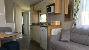 A compact living space with a kitchenette, a sofa, a dining table, and a small refrigerator. - The Leas Beach Park (Norwich)