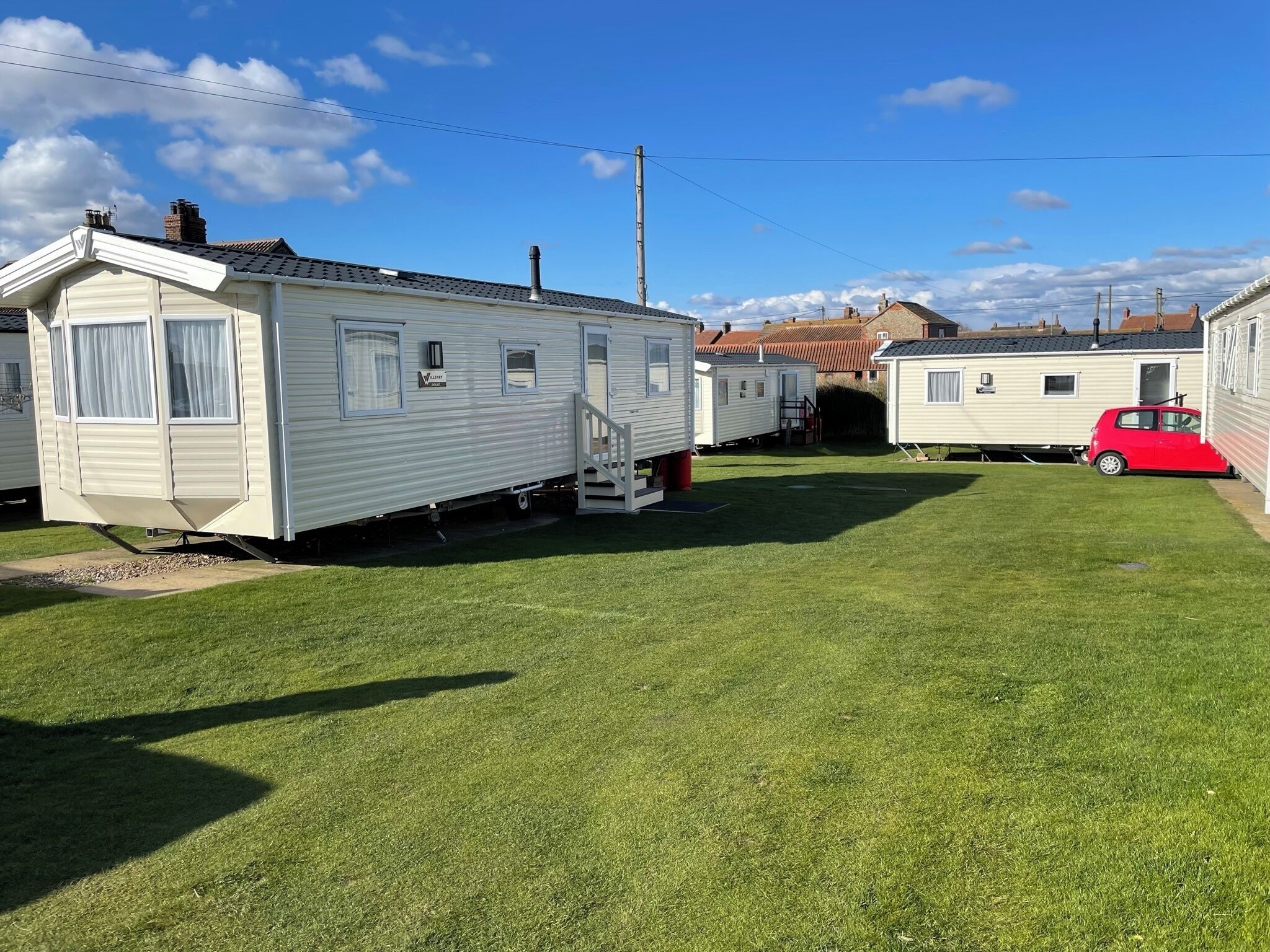 A row of mobile homes with a grassy yard and a red car parked nearby.