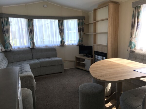 A living room with a grey sofa, a wooden table, and a TV on a wooden stand. - The Leas Beach Park (Norwich)