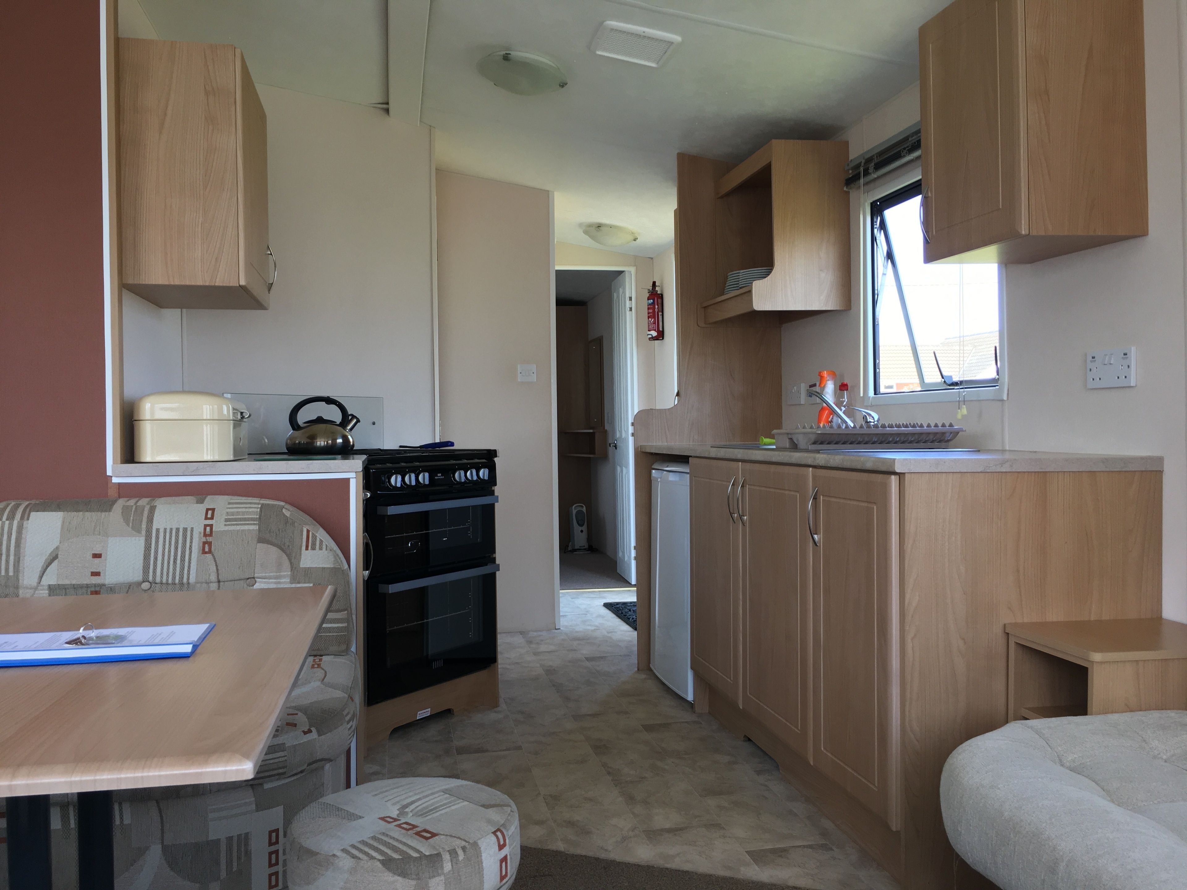 Cocina compacta para autocaravana con armarios de madera, estufa, pileta y un refrigerador pequeño.