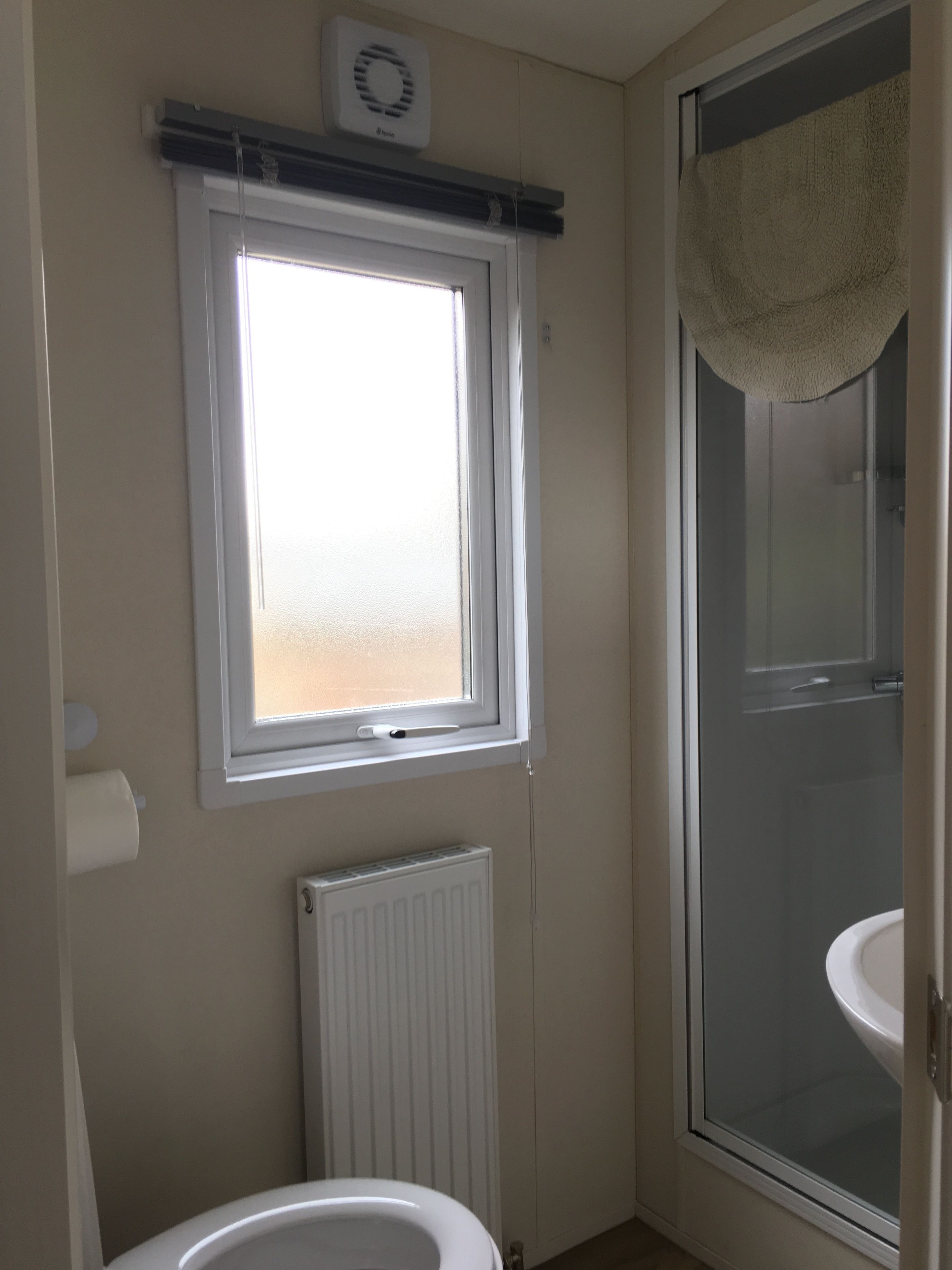 A bathroom with a window, a radiator, and a shower.