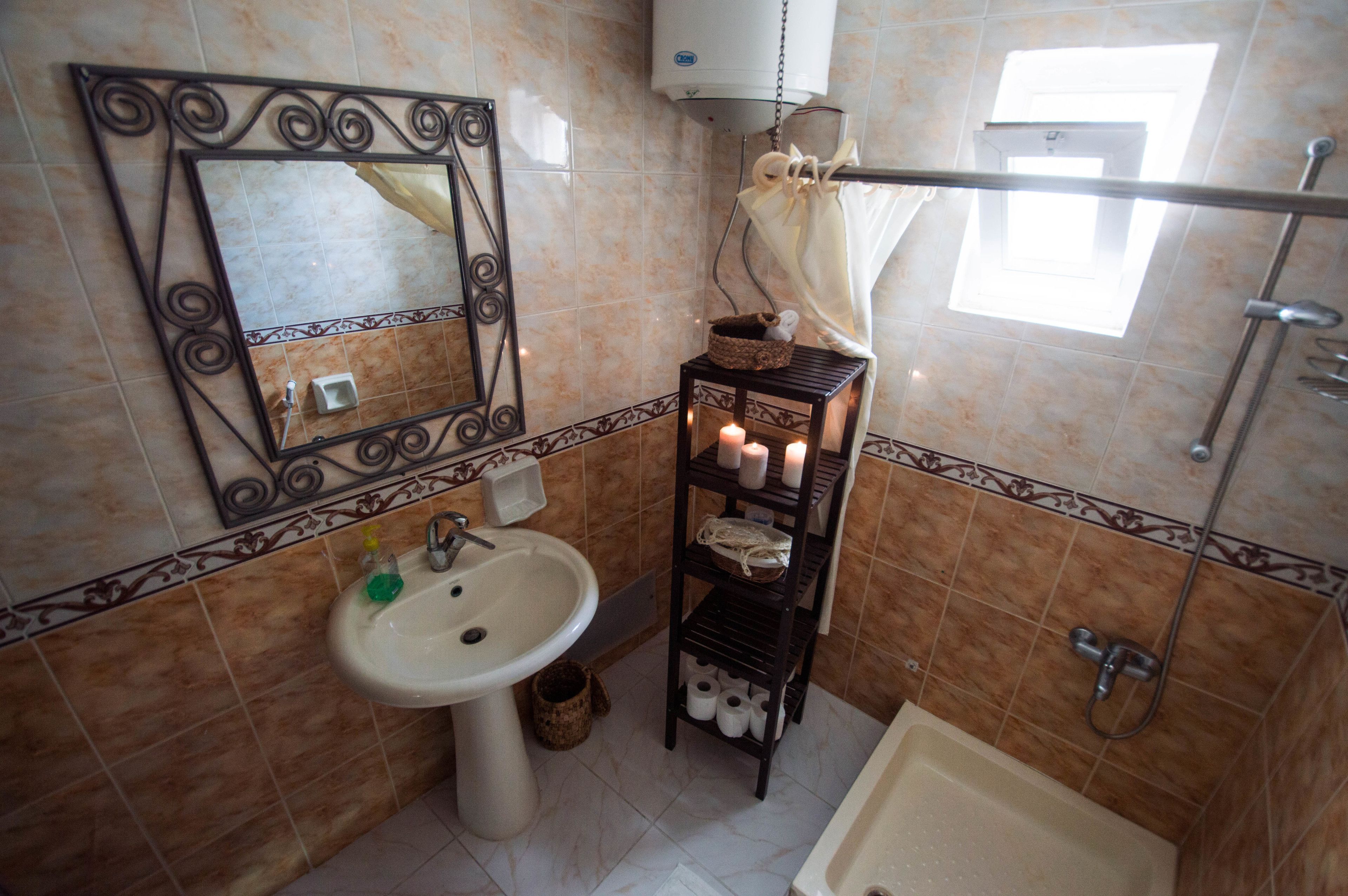 Un baño con lavamanos, espejo, repisa con velas y ducha.