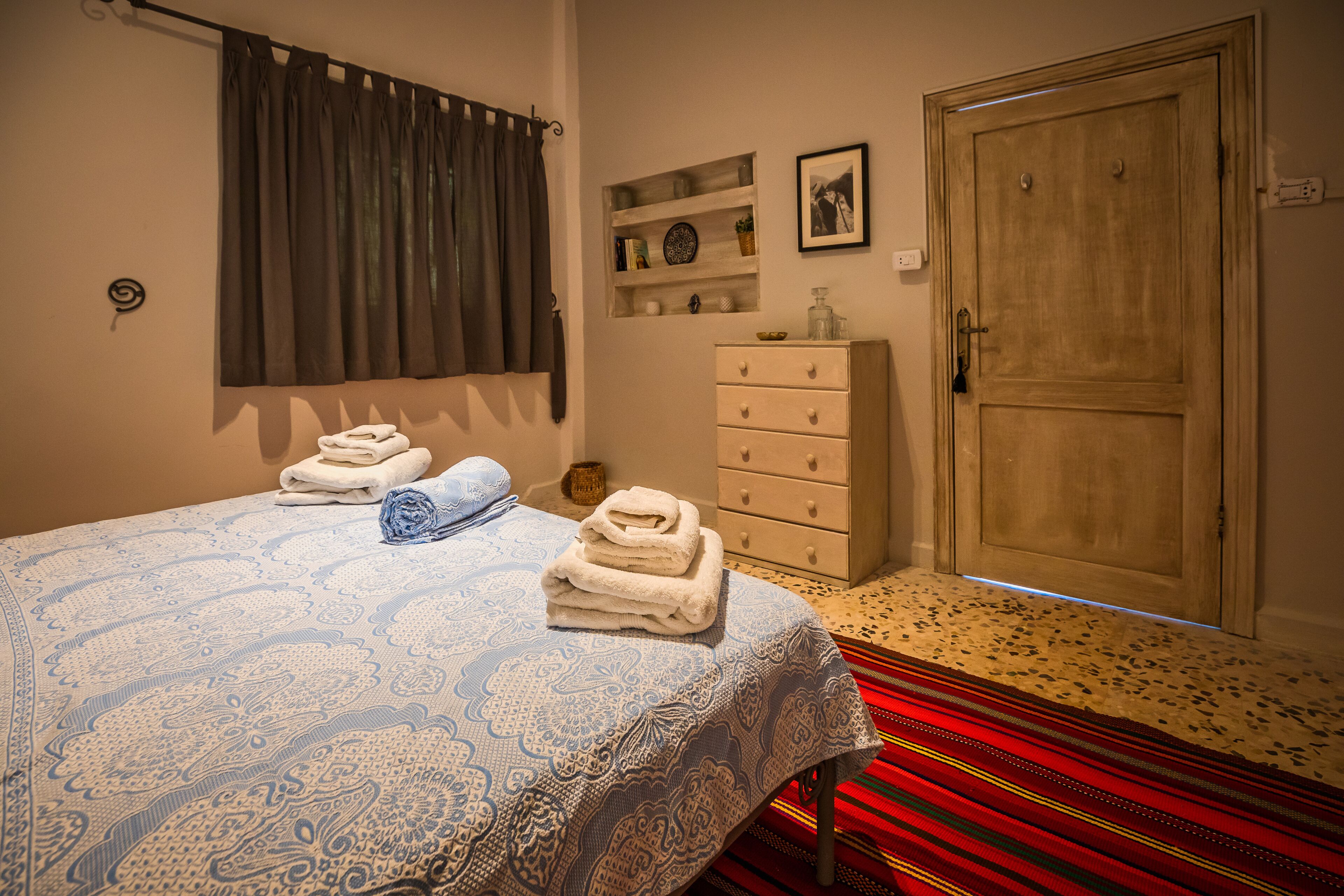 Quarto com cama, penteadeira, porta e janela com cortinas.