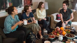 Un grupo de personas sentadas en un sofá en una sala de estar con una mesa de centro frente a ellas.