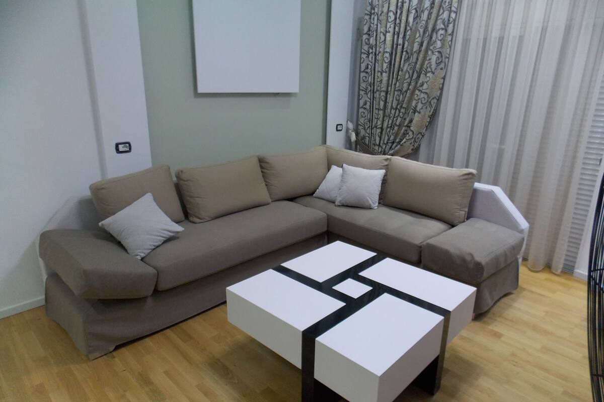 A modern living room with a sectional sofa, a coffee table, and a large window with curtains.