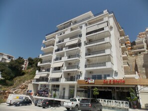 A multi-story building with balconies, a restaurant named "Le 5 Stelle" on the ground floor, and several parked vehicles including a van and cars. - Doka Apartments (Sarandë)