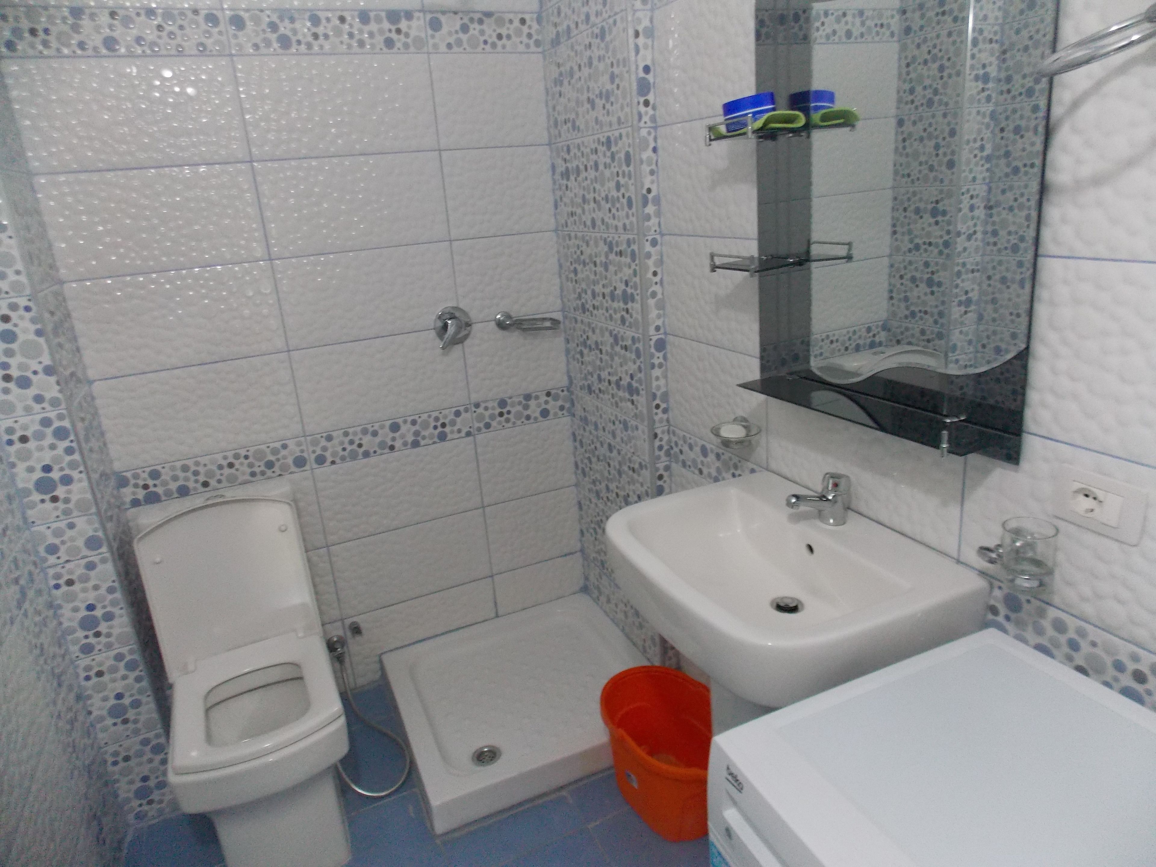 Une salle de bain équipée de toilettes, d’un bidet, d’un lavabo et d’un petit seau orange.
