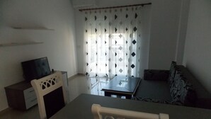 A small, sparsely furnished living area with a television, a sofa, and a dining table. - Doka Apartments (Sarandë)