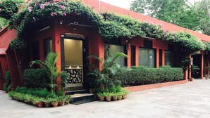 A building with a red facade, a gated entrance, and potted plants around the entrance. - Hotel Sheela (Agra)
