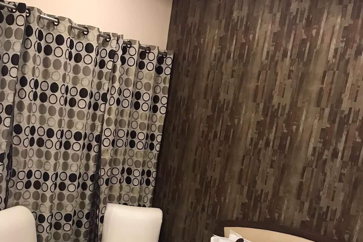 A hotel room with a bed, white pillows, a floral bedspread, and a curtain with a polka dot pattern.