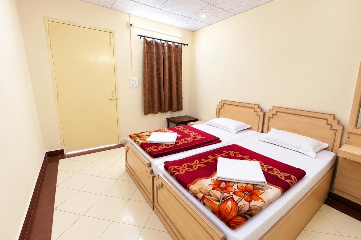 A hotel room with a double bed, two bedside tables, a wooden headboard, a window with curtains, and a door.