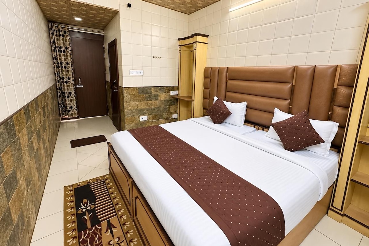 A hotel room with a large bed, a wooden headboard, a patterned rug, and a stone accent wall.