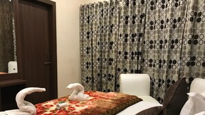 A hotel room with a bed, a chair, and a curtain with a circular pattern. - Hotel Sheela (Agra)