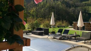 Un espace piscine agrémenté de chaises longues et de parasols, entouré de verdure et de collines.