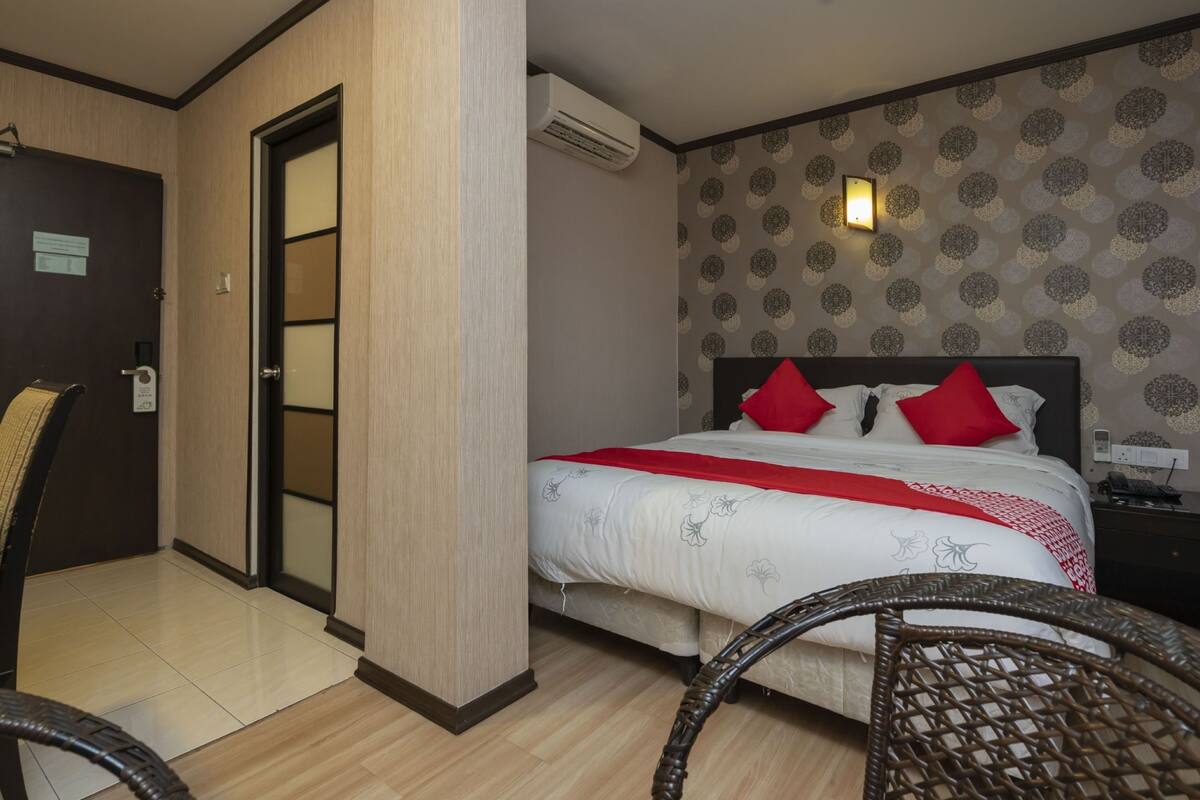 A hotel room with a bed, a chair, a door, and an air conditioning unit.