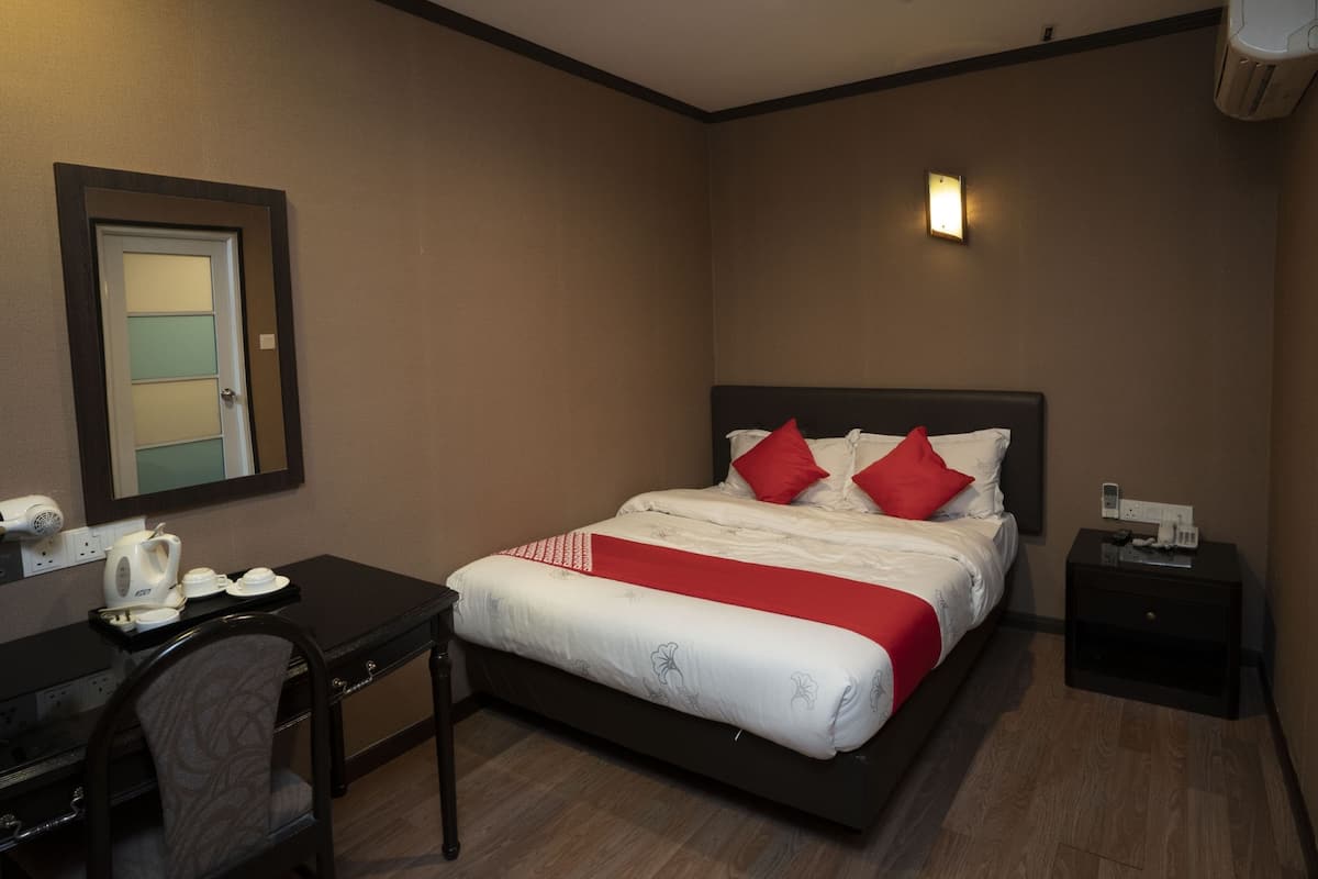A hotel room with a bed, bedside table, chair, and a desk with a kettle and cups.