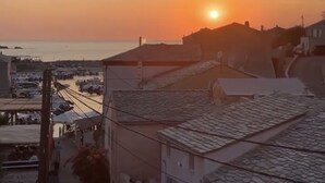 Un pueblo costero al atardecer con edificios y un puerto deportivo.