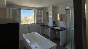 Un baño moderno con una bañera independiente, cabina de ducha y ventana con vistas a la ciudad.