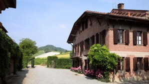 A traditional brick building with a gravel driveway, surrounded by greenery and hills in the background. - Tenuta Guazzaura (Serralunga di Crea)
