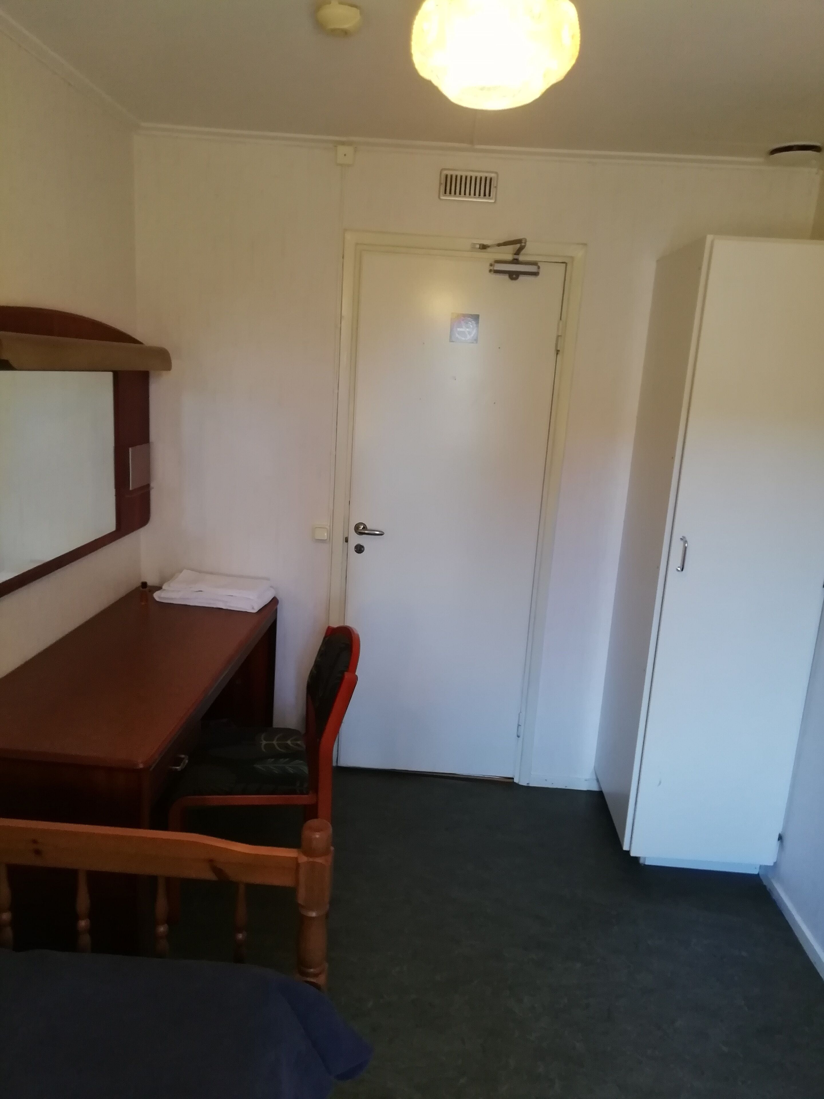 A room with a wooden desk, a chair, a white door, and a white wardrobe.