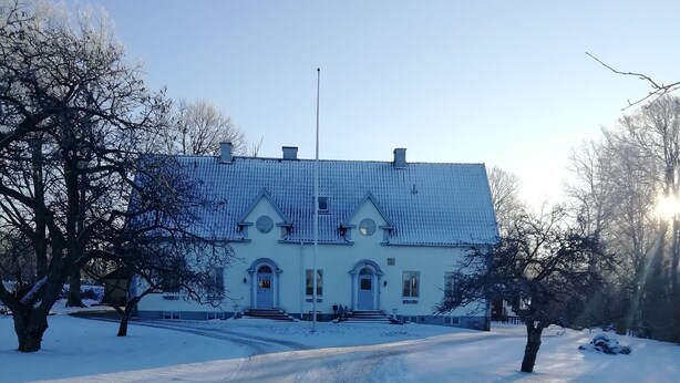 A snow-covered road leading to a large, white building with a symmetrical facade and a central entrance.