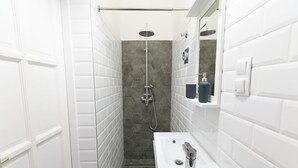 Ein modernes Badezimmer mit weiß gefliesten Wänden, einer Duschwand aus grau-hexagonalen Fliesen, einem weißen Waschbecken mit chromfarbenen Armaturen und einem Spiegel über dem Waschbecken.