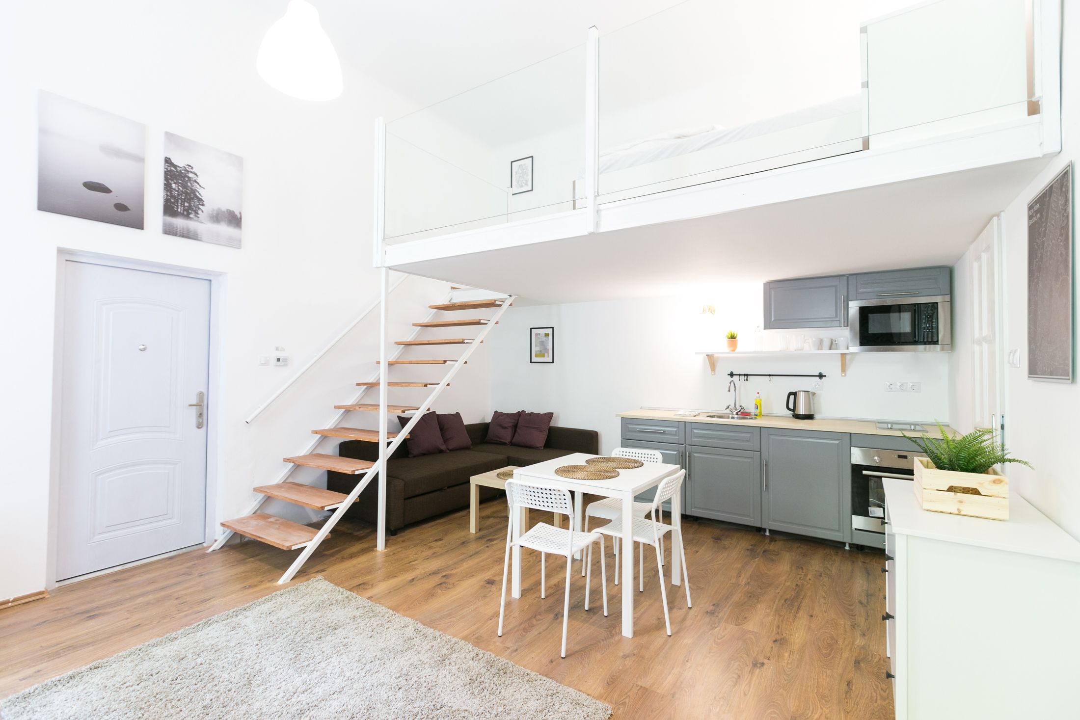 A compact living space with a staircase leading to an upper level, a kitchenette, a dining area, and a sofa.