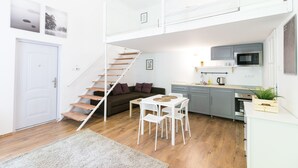 Ein kompakter Wohnraum mit einer Treppe zu einer erhöhten Ebene, einer Küchenzeile, einem Essbereich und einem Sofa.