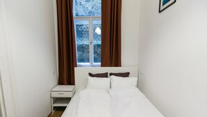 Une chambre à coucher avec un lit, une table de chevet, une fenêtre avec des rideaux et un tableau accroché au mur.