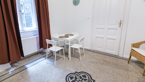 Une pièce avec une table blanche et quatre chaises, une porte portant un numéro et une fenêtre avec des rideaux.