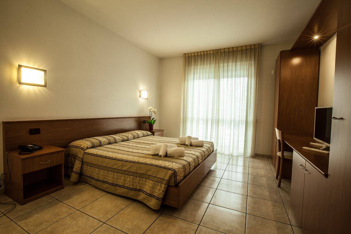 A hotel room with a large bed, bedside tables, a TV, and a window with curtains.