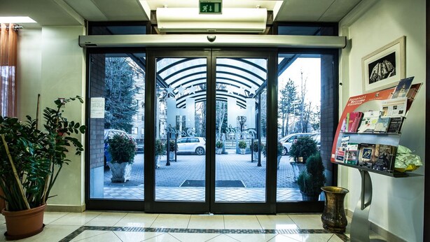 Ingresso di un hotel con porta girevole, piante in vaso e una reception con brochure informative.