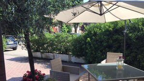 Patio esterno con mobili in vimini, un tavolo in vetro e una pianta in vaso.