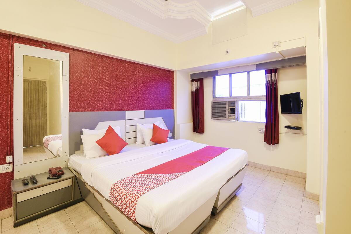 A hotel room with a bed, a TV, a mirror, and a ceiling fan.