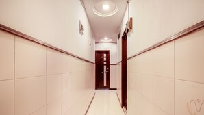 A corridor with white tiled walls and a shiny floor, leading to a door at the end. - OYO Flagship 12273 Hotel Indraprastha (Chhatrapati Sambhajinagar)