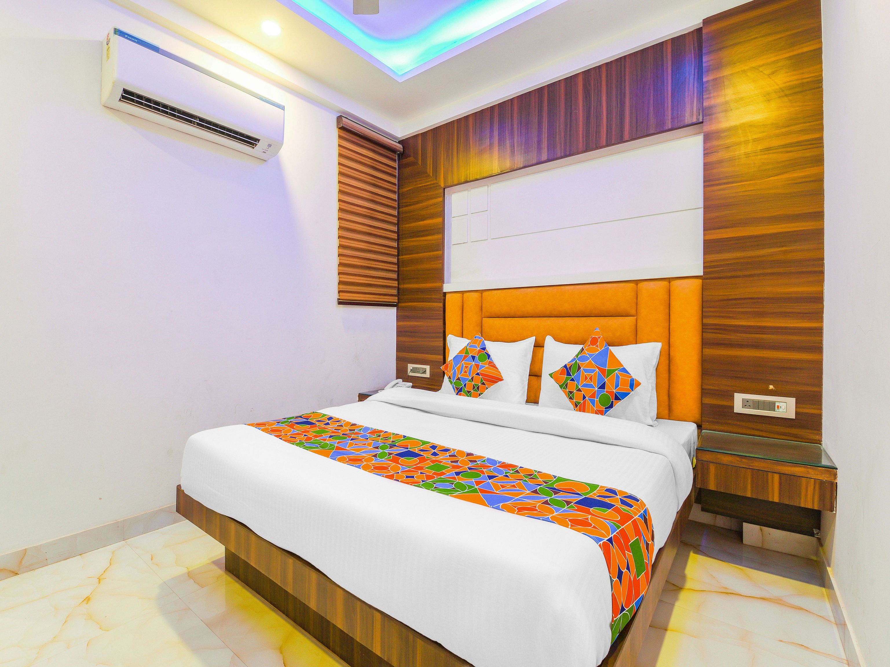 Ein modernes Hotelzimmer mit einem großen Bett, einem Holz-Kopfteil und einer farbenfrohen Bettdecke.