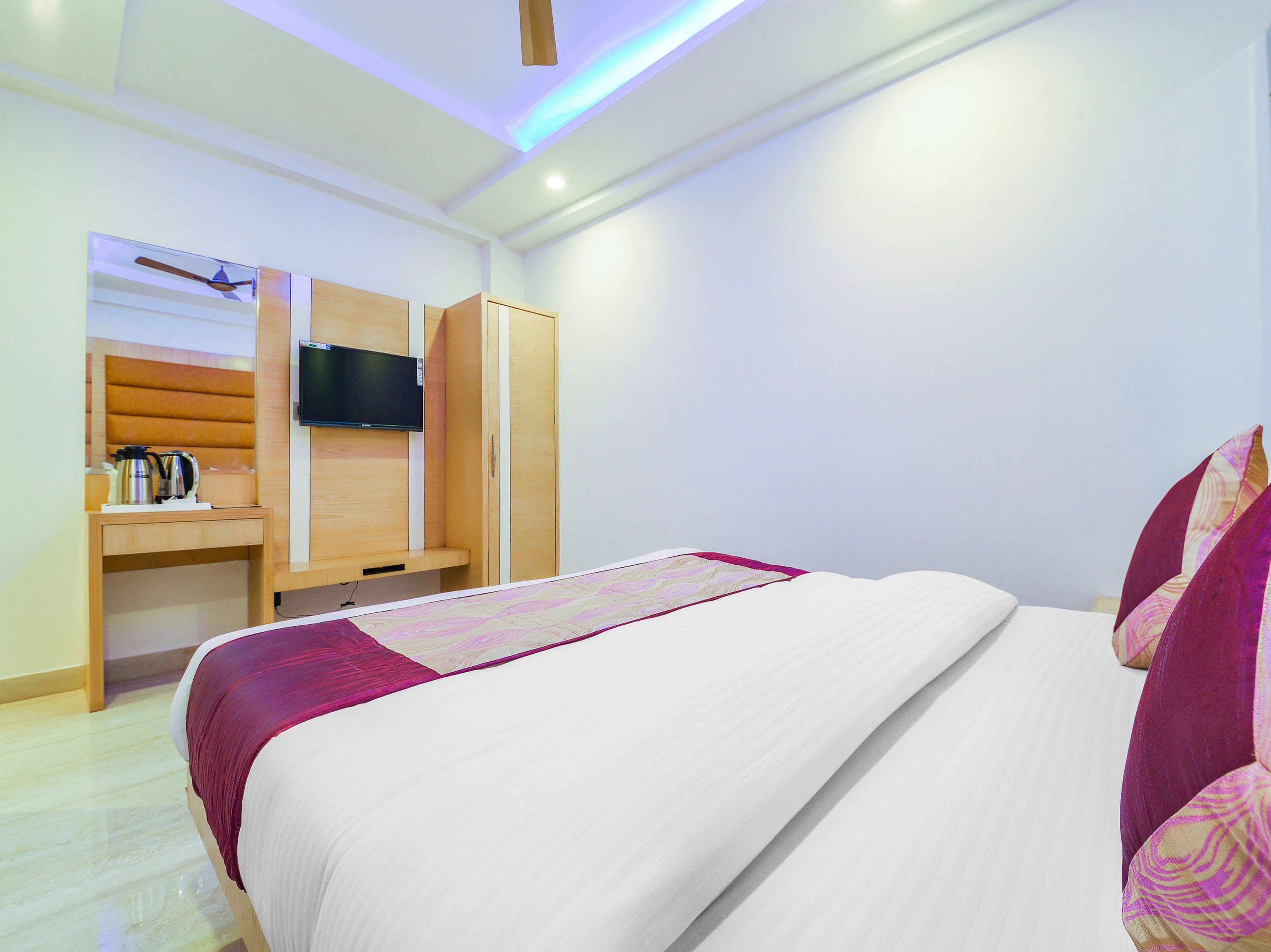 Une chambre d’hôtel avec un lit, un téléviseur fixé au mur, une armoire en bois et une machine à café sur la table de chevet.