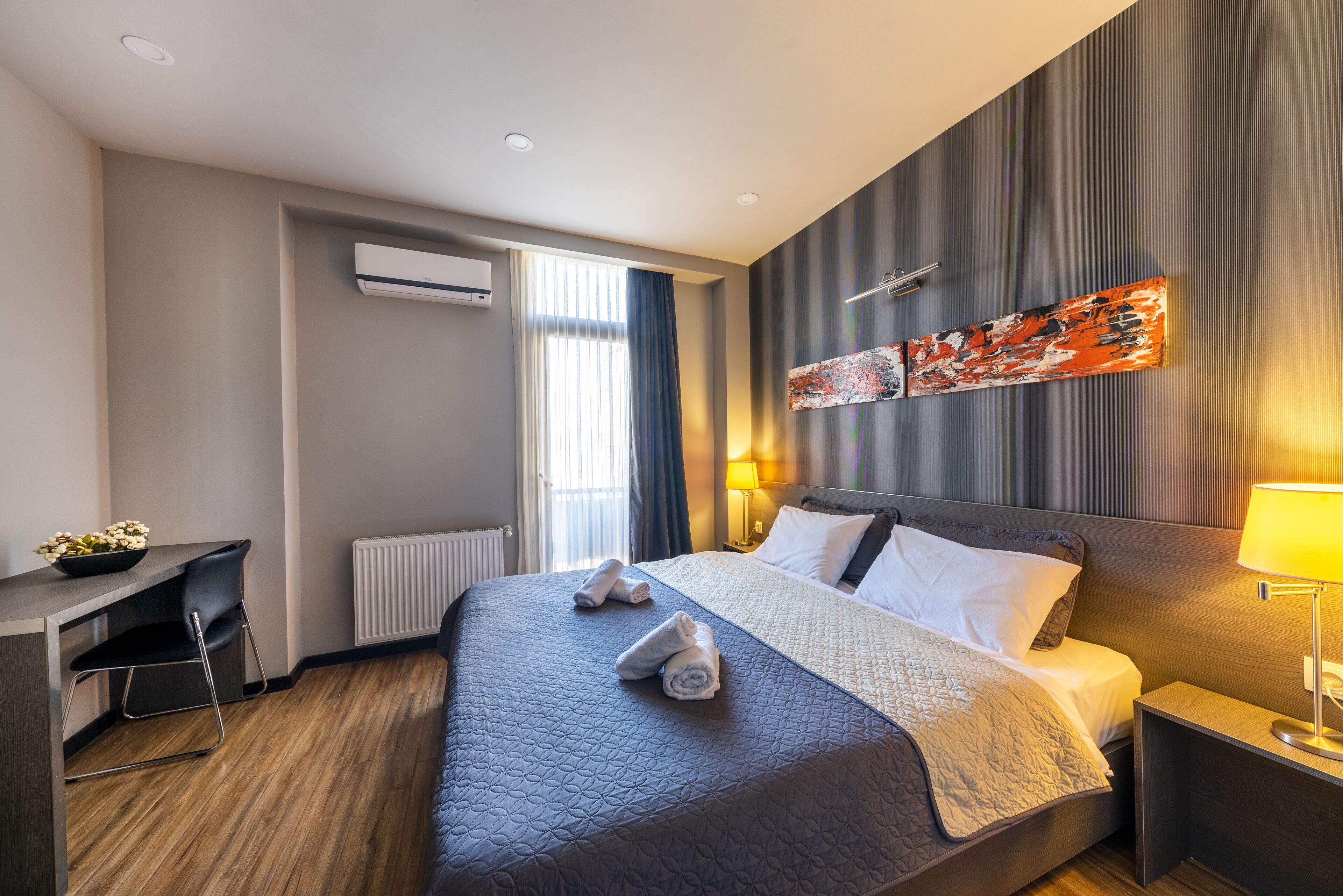 A modern hotel room with a large bed, a desk, and a wall-mounted air conditioner.