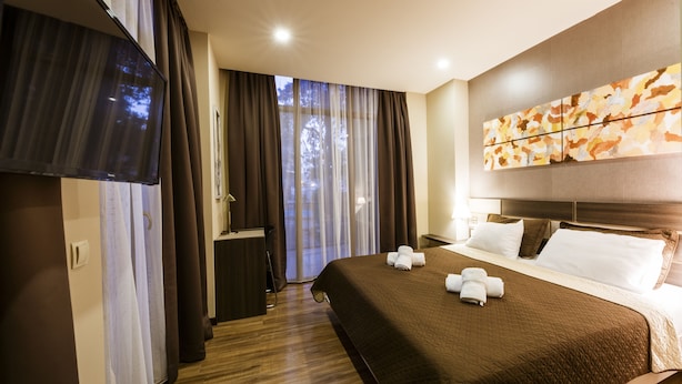 A hotel room with a large bed, a flat-screen TV, a desk, and a window with curtains.