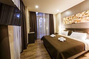 A hotel room with a large bed, a flat-screen TV, a desk, and a window with curtains.