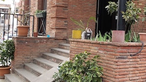 A brick building with a covered entrance, steps leading up to a door, and several potted plants around the entrance area.