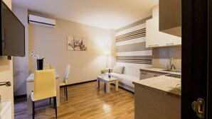 A modern living room with a sofa, a dining table with chairs, a coffee table, and a kitchen area with a sink and cabinets.