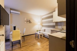 A modern living room with a sofa, a dining table with chairs, a coffee table, and a kitchen area with a sink and cabinets.