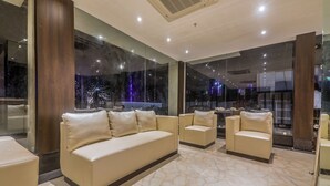 A modern hotel lobby with a large beige sofa, smaller armchairs, and a marble floor. - OYO 16719 Airport Guest House (Guwahati)