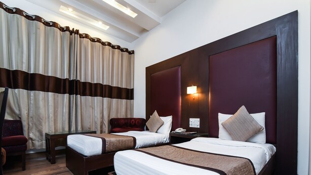 A hotel room with two beds, a nightstand, a desk, a chair, and a large window with curtains. - OYO 644 Hotel Haris Court (Gurugram)
