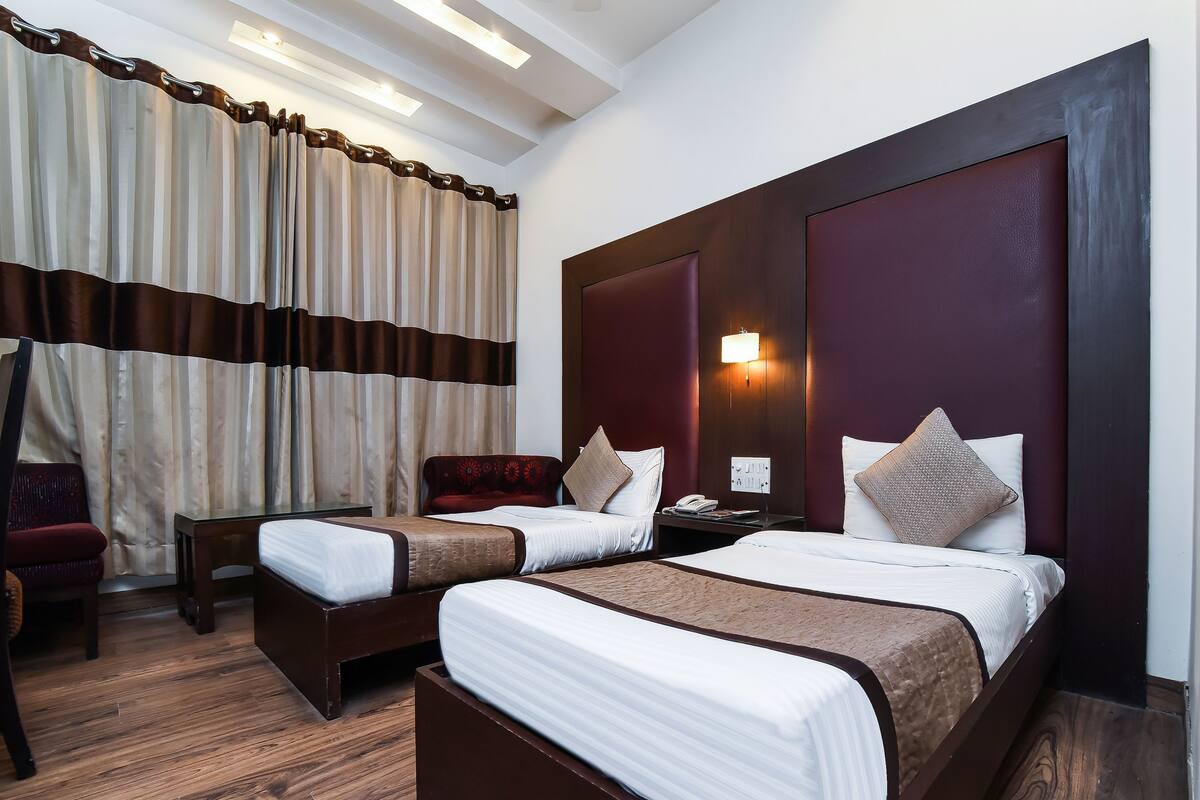 Ein Hotelzimmer mit zwei Betten, einem Nachttisch, einem Schreibtisch, einem Stuhl und einem großen Fenster mit Vorhängen.