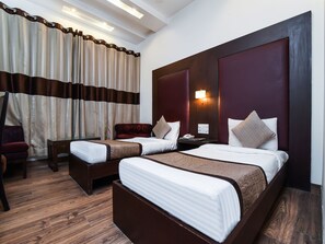 A hotel room with two beds, a nightstand, a desk, a chair, and a large window with curtains. - OYO 644 Hotel Haris Court (Gurugram)