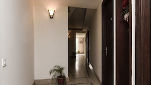 A hallway with a potted plant, a wall-mounted light fixture, and a door with a floral decoration. - OYO 644 Hotel Haris Court (Gurugram)