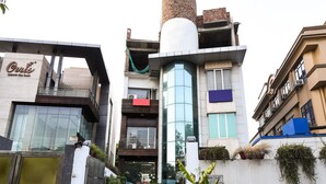 A modern building with a glass facade, a cylindrical structure on the roof, and a sign reading "Aris Court." - OYO 644 Hotel Haris Court (Gurugram)