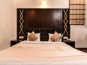 A neatly made bed with a lace bed skirt, a wooden headboard with a geometric pattern, and two bedside tables with lamps. - OYO 644 Hotel Haris Court (Gurugram)